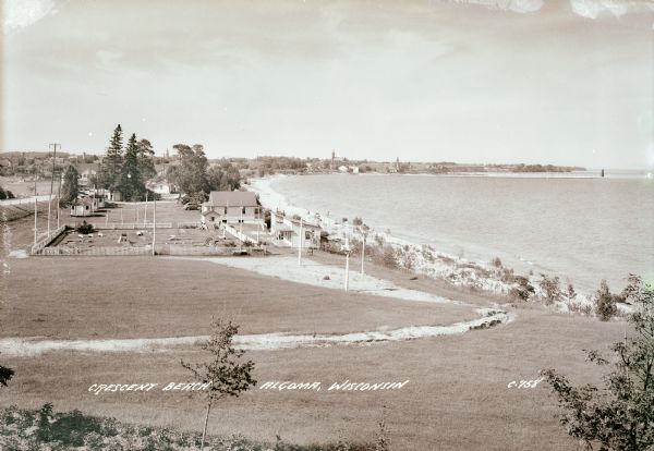 Elevated view of Crescent Beach, with campsite with cabins and miniature golf course and other outbuildings. Downtown buildings can be seen in the background.