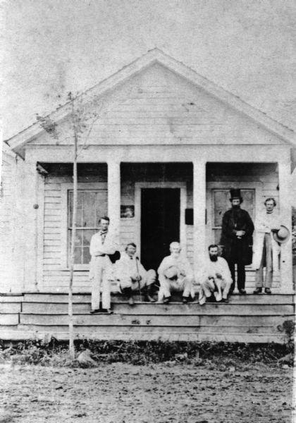 Jeremiah M. Rusk, in black, standing on the porch of the C.M. Butt law office.  They are, seated left to right, Judge Carson Graham, Judge James Evans Newell, and Cyrus M. Butt; Standing left to right: Royal Clifton Bierce and Judge William F. Terhune. Rusk later became governor of Wisconsin and the first secretary of Agriculture.