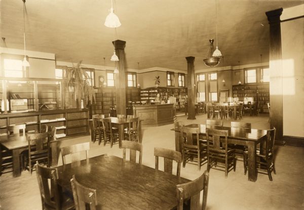 Interior view of the Sturgeon Bay Public Library. Prominent elements are reading tables, librarian's desk, bookshelves.