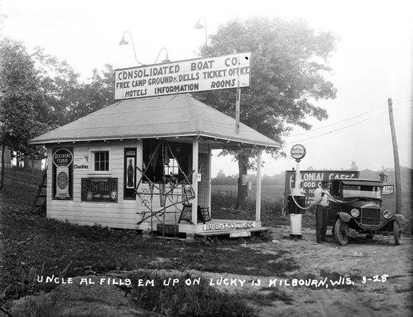 Man pumps gas into an automobile at the Consolidated Boat Co. There is advertising for Coca-Cola, Baby Ruth, and Occident Flour on the side of the small frame building.