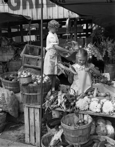 Two girls selecting vegetables at an open air market.