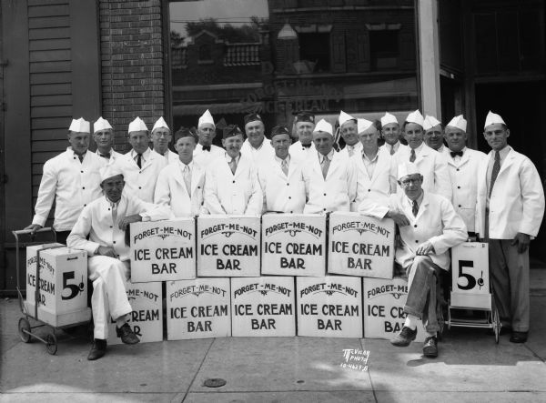 Group portrait of 22 disabled American veterans who are Forget-Me-Not ice cream bars vendors. They are posing in front of 503 State Street with boxes of ice cream bars which they sell from a small refrigerator cart on wheels. The ice cream mix is produced at the University of Wisconsin-Madison, and the ice cream is manufactured by the Crystal Products Co., 412 West Gilman Street.