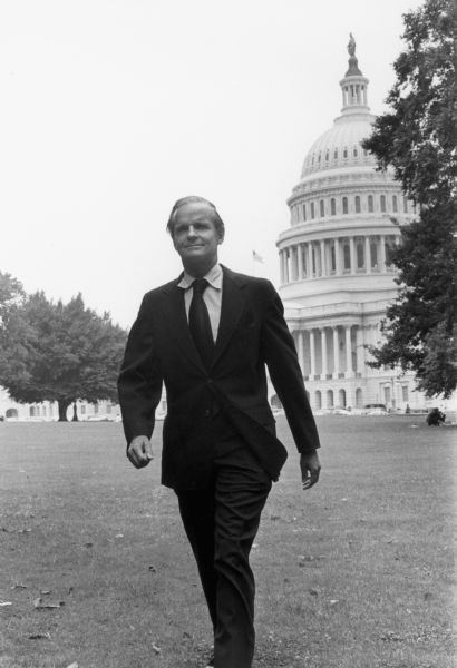 Senator William Proxmire strolls on the Capitol lawn wearing a suit and necktie.