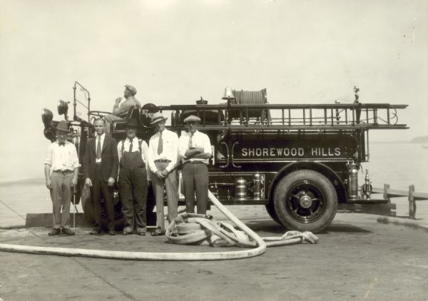 Members of Shorewood Fire Fighters standing in front of fire engine posing outdoors near a lake.