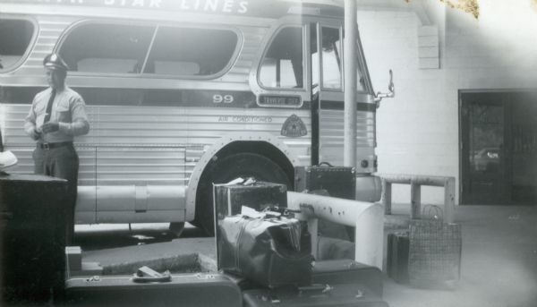 A Greyhound bus driver collects tickets while standing in front of his bus en route to Traverse City. There are several pieces of luggage in front of the bus.