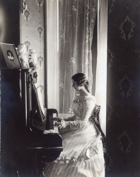 A young woman (Grace) plays music while seated at the piano.