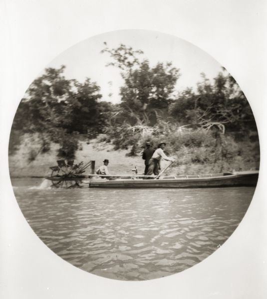 View on the Ohio River of a skiff with a small paddle wheel at the stern. There are three men aboard the boat.