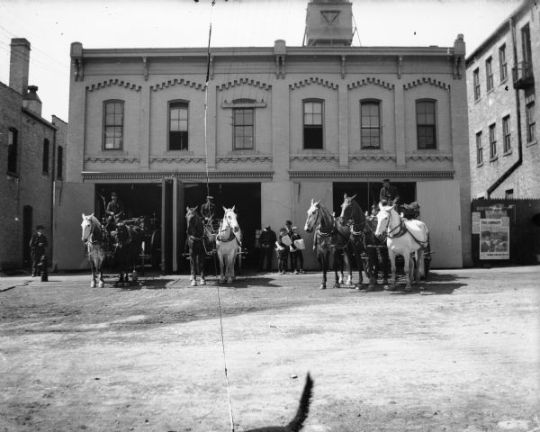 Madison old Central Fire Station (1881-1904), 10 South Webster St. Three men driving horse-drawn ladder trucks in front of Madison Fire Station, 10 S. Webster St. Two boys in the background are holding stacks of newspapers.