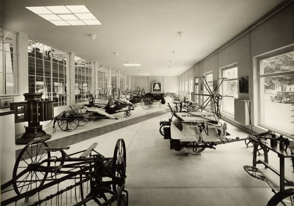 Grain binder and other farm equipment in the showroom at International Harvester's Berlin-Tempelhof branch house in Germany. On the left is a circular wooden display case containing photographs of tractors.