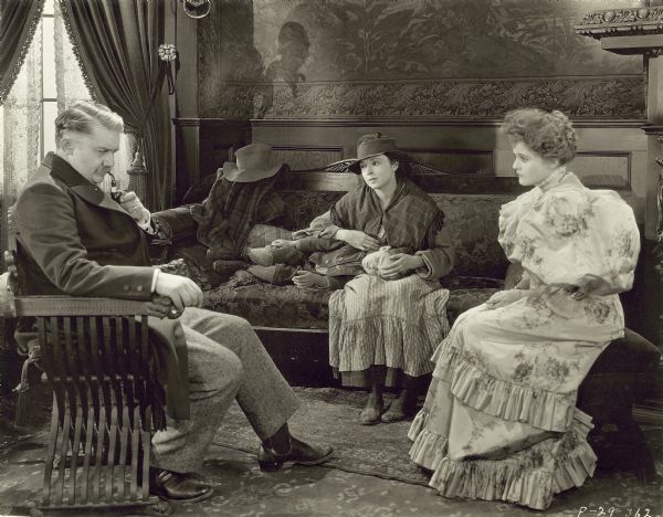 A scene from the film "So Big" in which Jean Hersholt (left), Colleen Moore sitting on couch with a child laying his head in her lap, and Charlotte Merriam (right) seated in a living room.