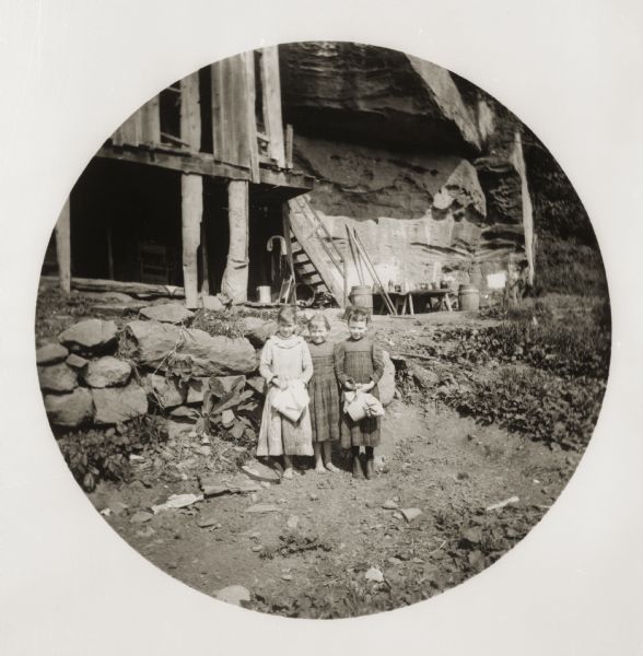 Three little girls pose in front of a house built next to a cliff.