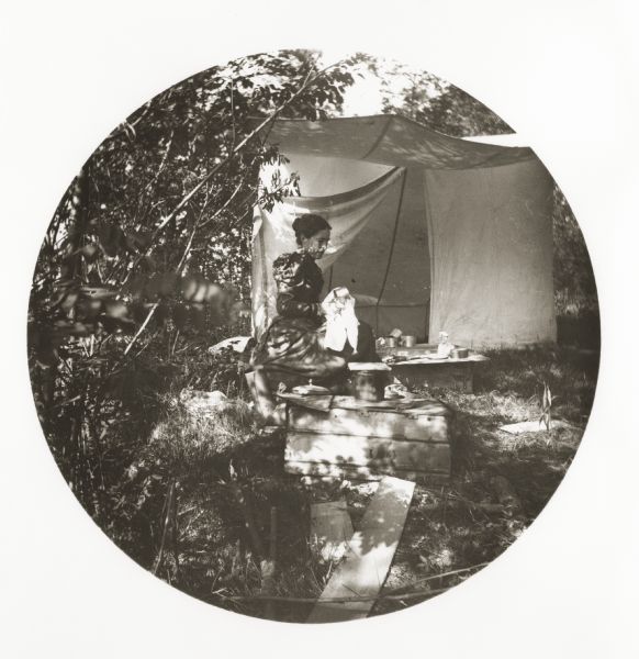 Jessie Thwaites seated outdoors near a tent wiping dishes.