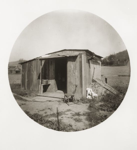Exterior view of a rundown oil worker's shanty, with a chair near the doorway.