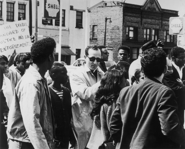 Father James Groppi, seen wearing sunglasses in the middle of a crowd, leads a demonstration against discrimination.
