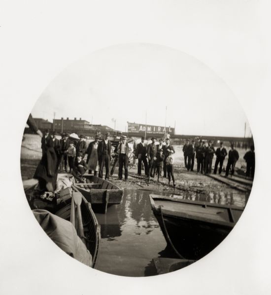 A crowd of people gathered on a wharf with boats in the foreground.