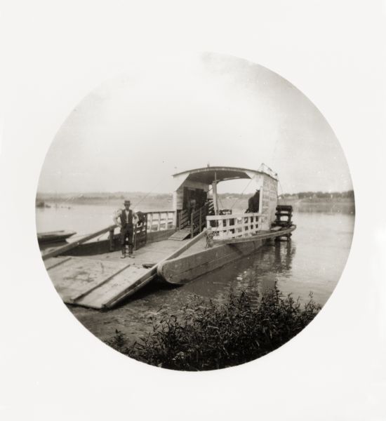 A ferryman poses on his docked ferry. Two horses are loaded on the ferry.