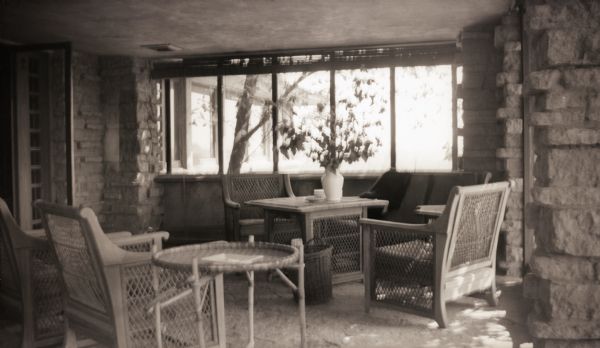 Wicker chairs and tables at Taliesin, the summer home of architect Frank Lloyd Wright and the Taliesin Fellowship.  The furniture is in front of a wall of windows.  The floor and walls are stone. Taliesin is located in the vicinity of Spring Green, Wisconsin.