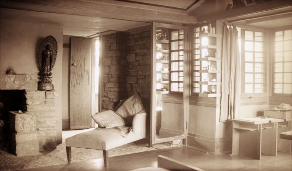 A portion of the fireplace and windows in the bedroom of Olgivanna Wright at Taliesin, the summer home of Frank Lloyd Wright and the Taliesin Fellowship.  A chaise lounge is in front of the fireplace and there are built-ins under the windows. Taliesin is located in the vicinity of Spring Green, Wisconsin.