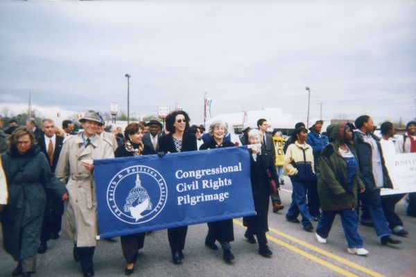 A group of people holding a banner while marching down a road as they take part in the Faith and Politics Congressional Civil Rights Pilgrimage to Selma.