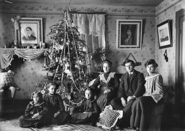 A family dressed in formal clothing seated around a Christmas tree in the living room.