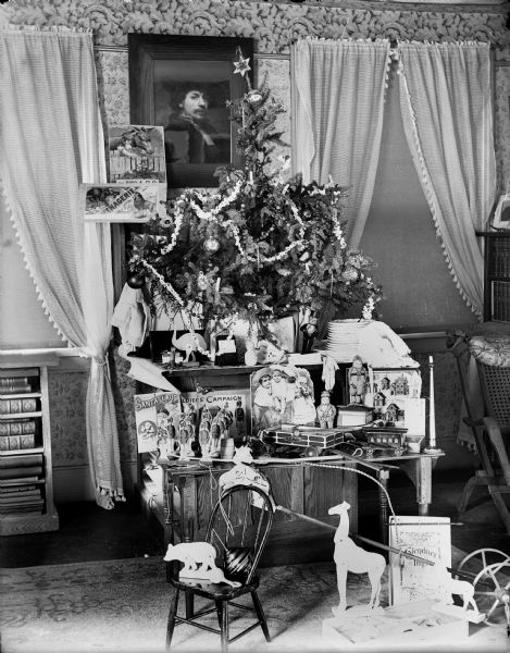 Christmas tree on a tabletop display in a living room, possibly in the home of Frederick King Conover. There are toys on the table and a small chair with more toys on the floor in front of the tree.