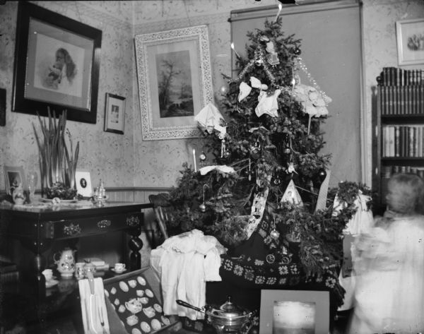 Child with a Christmas tree and presents in a house.
