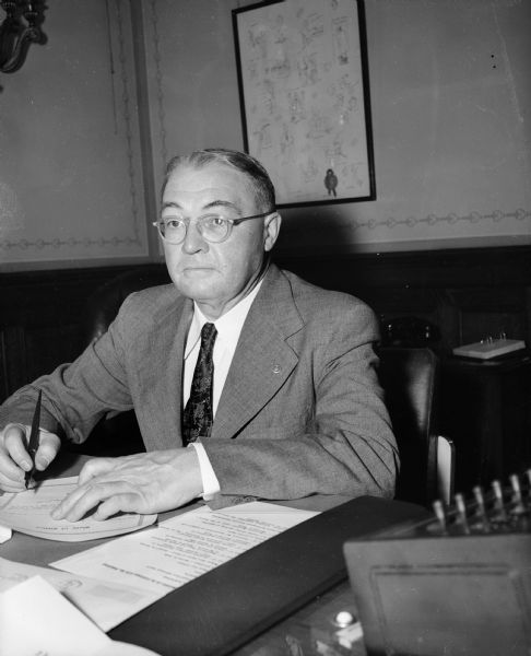 Attorney General Grover Broadfoot is shown seated, signing a document.
