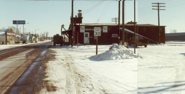 Main Street (USH 10) in the village, with storefronts and a used car dealership.