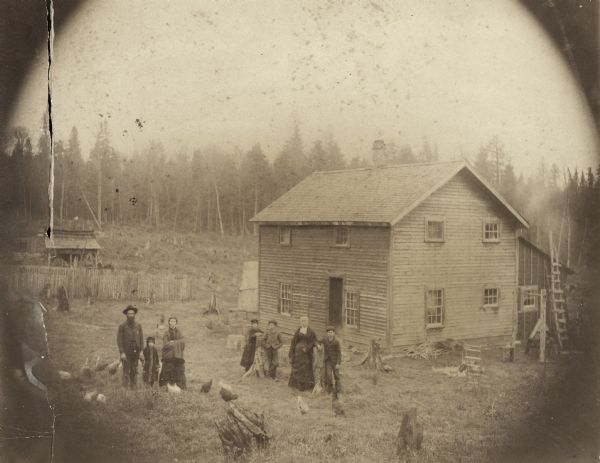 Mosher family standing in front of the J.F. Mosher residence. From the left are J.F. Mosher, daughters Celia Belle, Rhoda Adelaide, and Bertha May, son Herbert Harris, wife Jane McMillan, and son Justice Henry. In the yard are tree stumps and chickens.