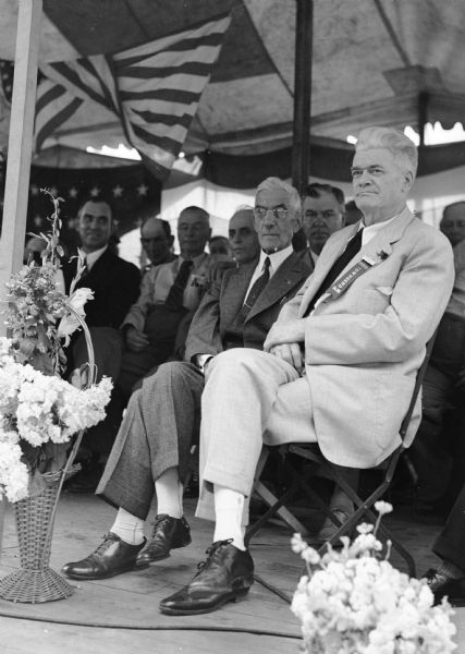 Dr. Francis E. Townsend seated on the platform of a Townsend Plan Club at a park.