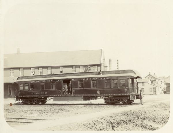 Exterior view of a fish stocking railroad car. Two men are standing at an open doorway of the car, and another man is standing on the ground on the right.