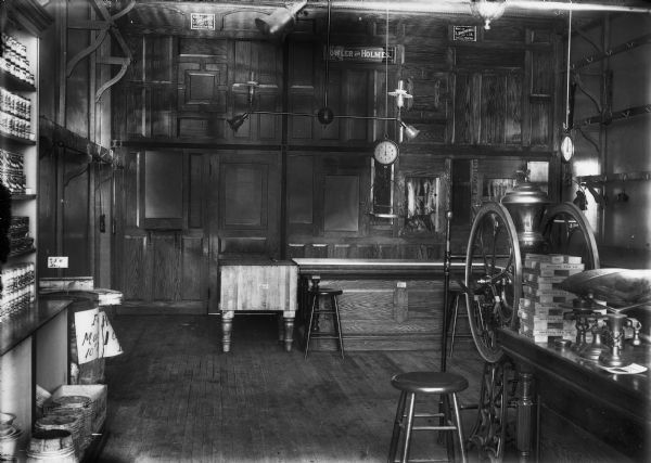 Interior view of the butcher shop section of the Fowler and Holmes Store. There is wood paneling and cabinetry throughout the room, shelving and hooks on the walls, a hanging scale, and a table scale on a table on the right.