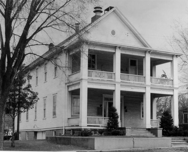 Exterior view of the Middleton Village Hall. There are porches on the first and second floors, and a bell is on the right side of the porch above the entrance.