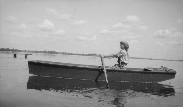 Mary Brandel rows a boat on a lake (possibly Fox Lake). There is a wooden pier in the background.