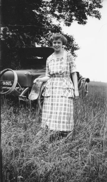 A woman poses outdoors near a parked car.