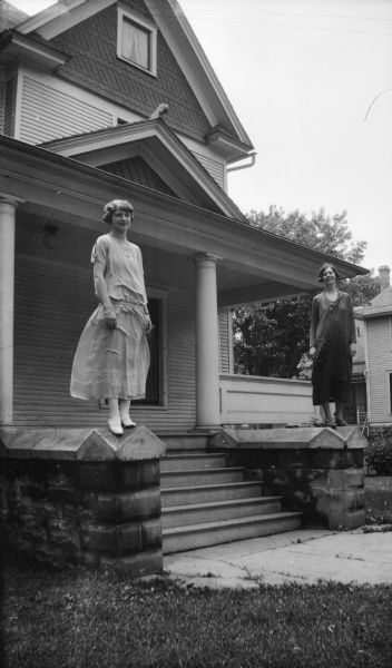 Mary Brandel and Lucille Laun pose outside the Brandel home. They are standing on top of the brick walls which frame the stairway to the front porch.