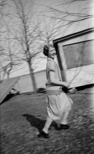 Mary Brandel is smiling and running in the yard. There is a cottage and lake in the background.