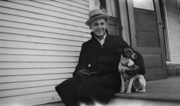 Harold Smith, wearing a hat, coat, and gloves, sits on a porch step with Max the dog. He is holding a pipe in his right hand.