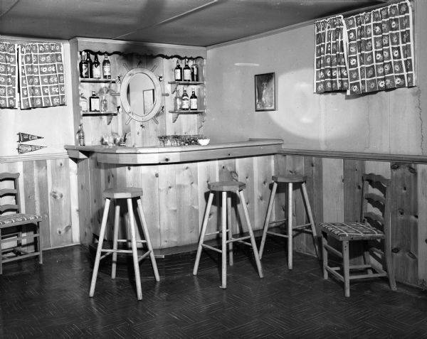 The knotty pine recreation room of Byron and Mary Burch house at 205 South Owen Drive. The room includes a bar with stools and a mirror in the shape of a ship's wheel.