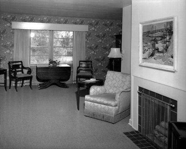 The living room of the Arthur H. Peterson house, 4175 Cherokee Drive. There is a fireplace on the right side and an upholstered chair and a table stand in the background.
