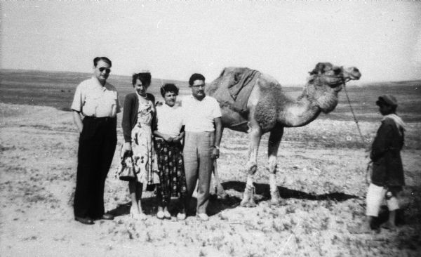 Eugene and Magda Herzberger (at left) with friends in the Negev region of Israel. They pose near a camel held on a tether by a man, possibly of Bedouin descent.
