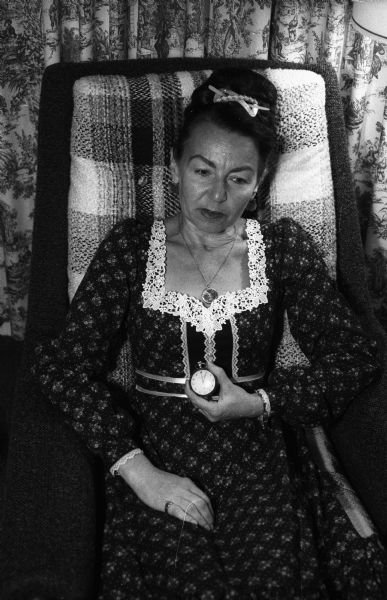 Magda Herzberger sits in an upholstered chair in her home holding the watch that was given to her father on the occasion of his Baccalaureate in Cluj, Romania, ca. 1915.
