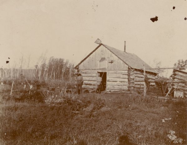 Two men in front of a log cabin hunting lodge.