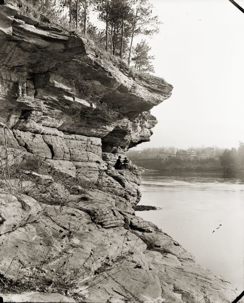 Woman and two girls on Angel Rock. There are buildings on the opposite side of the river. A bridge is in the distance.