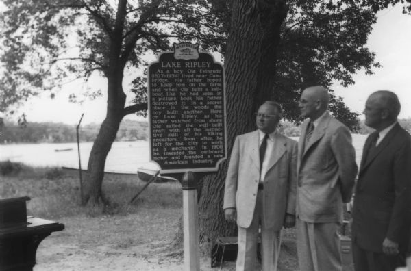 Arthur Melster, President of Cambridge Foundation; K.K. Amundson. M.D. of Cambridge; and W.T. Webb of Evinrude Motors, look at the Lake Ripley Ole Evinrude official historical marker in Lake Ripley Park.
