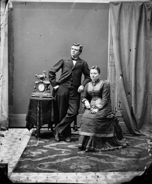 Studio portrait of photographer Gerhard Gesell, Sr. and his wife Christine Giesen Gesell taken shortly after their marriage in 1879. She is sitting in a chair, and he is standing and leaning on the back of the chair.