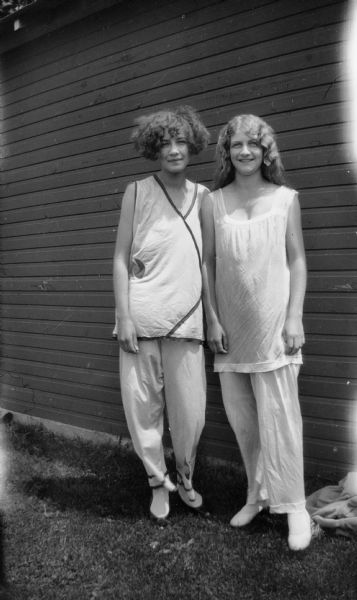 Muriel Markham and Mary Brandel pose outdoors together near the side of a building in what appear to be pajamas.