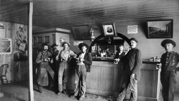Men standing along the bar of local saloon owned by Liegeois Brothers. Blacksmith Joseph Liegeois, Jr. and his brother John are on the end of the bar. John Leigeois was President of Abrams Bank for many years. Louis Liegeois is shown at the right end of the bar. A sign on the back of the bar says: "Meet Friendly, Drink Moderately, Pay on Delivery, Part Quietly, & Call Again."


