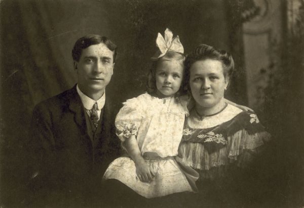 A studio portrait of one of the Eken brothers with his wife and young daughter.