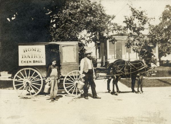 A man and a boy pose next to the horse-drawn Eken Brothers Home Dairy wagon. In the background is a house.